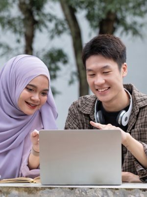 Happy multiethnic group of teenage students talking about the homework after the class at university campus. Two young people smiling, having a friendly conversation together.